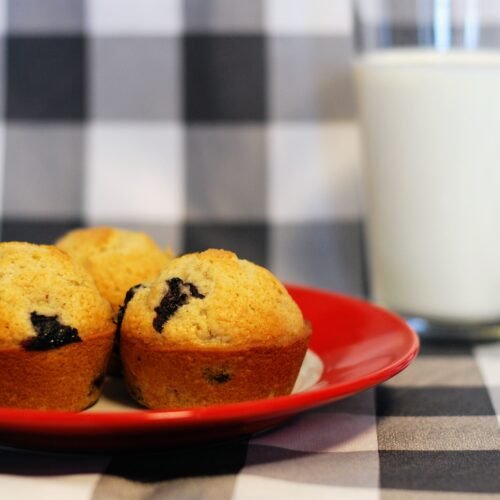 Three blueberry muffins with a glass of milk.